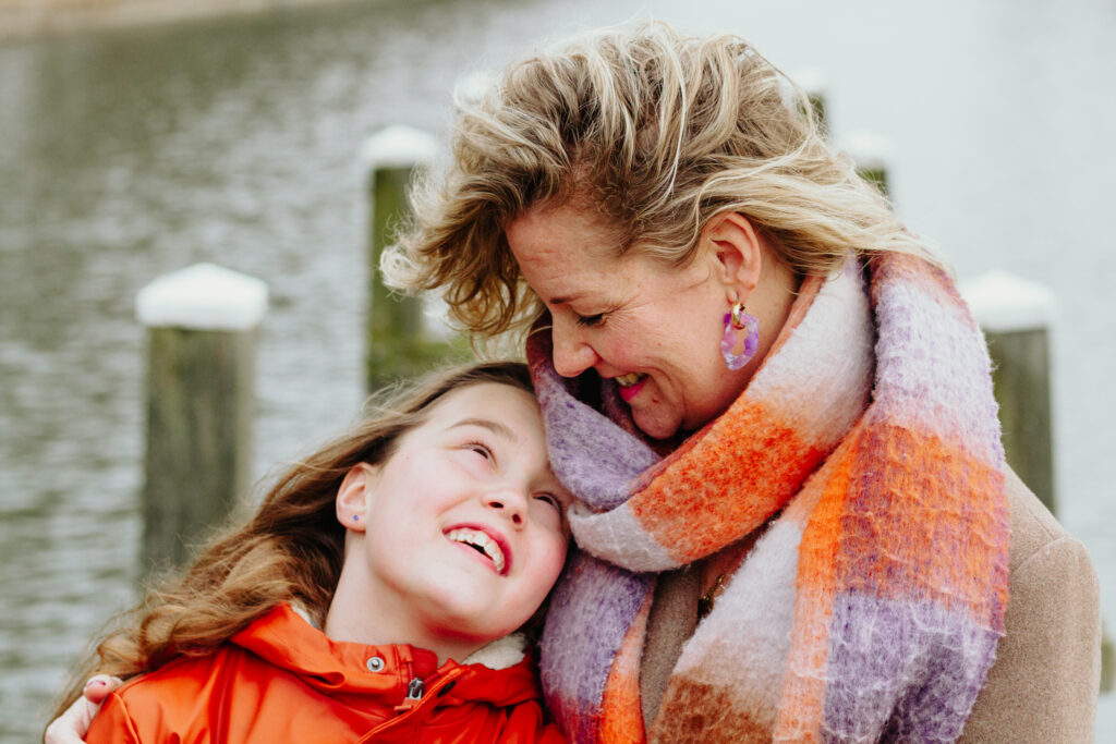 Moeder kijkt haar dochter lief aan tijdens een fotoshoot. Ze zitten op een steiger in Zwolle.